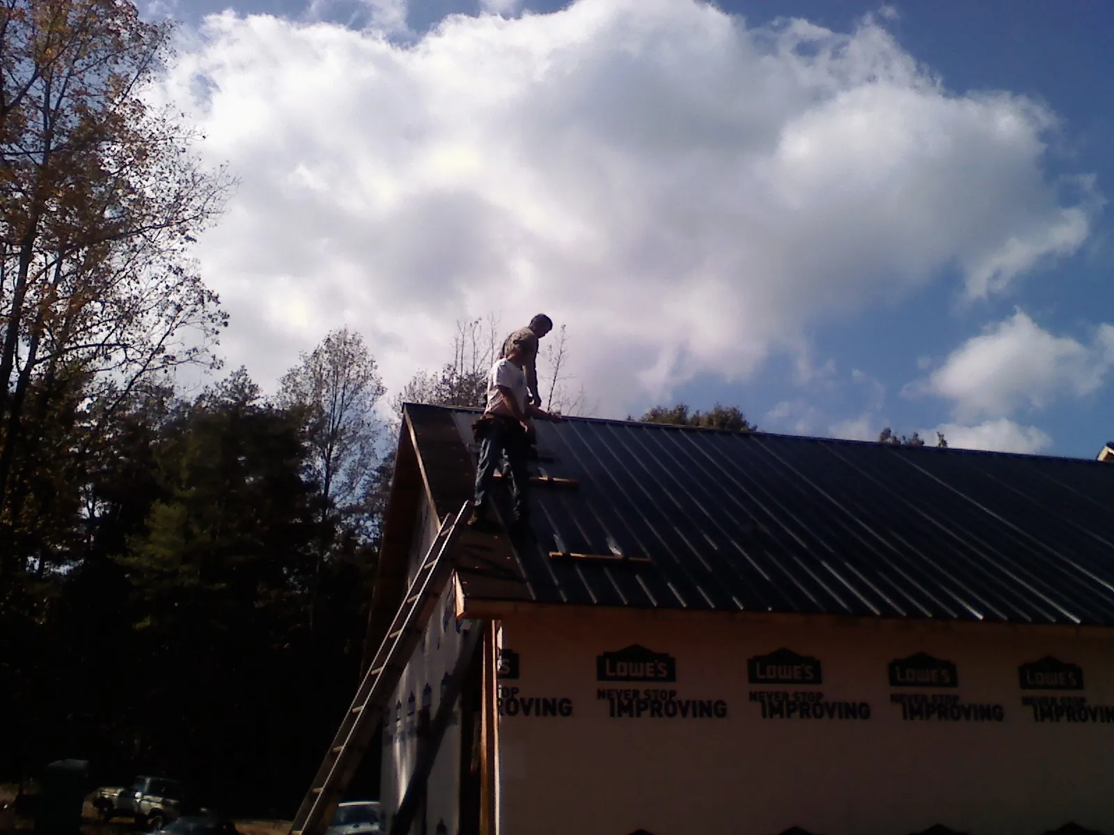 Roofer fastening dark metal panels high against a cloudy sky, from a Roof Inspection job in Bedford